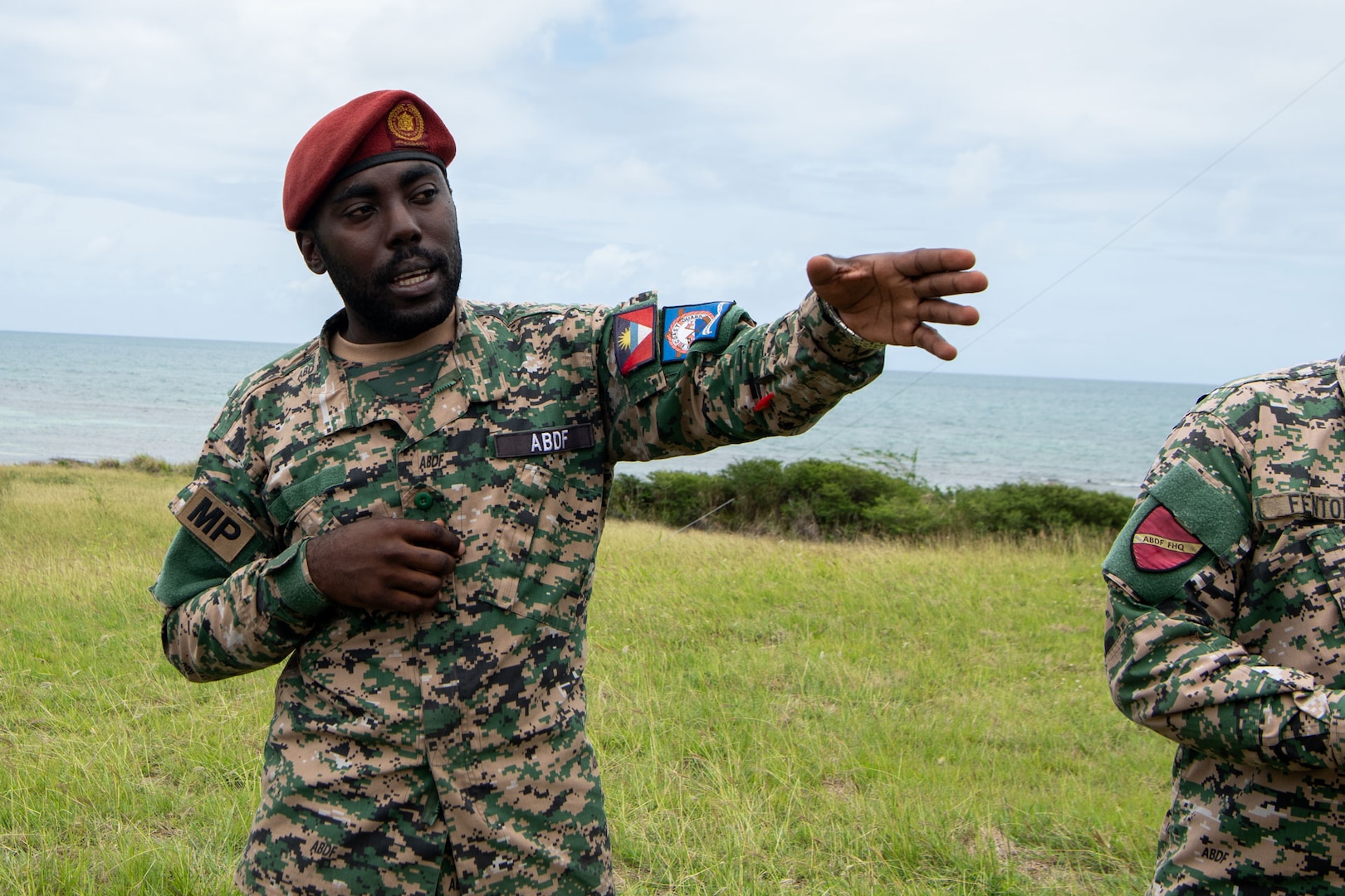 A man in an Antigua and Barbuda Defense Force uniform gestures to his left while facing the camera
