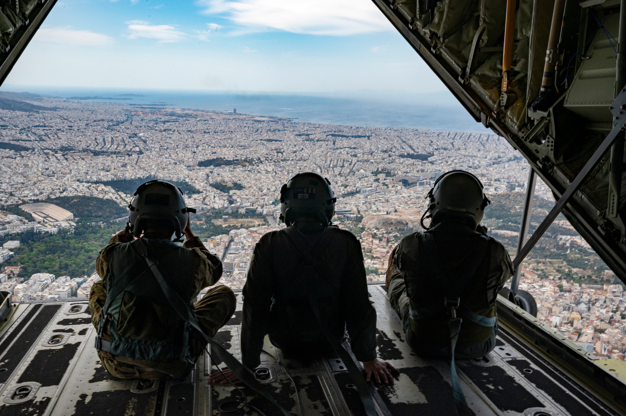 Two U.S. Airmen and a Hellenic Air Force member ramp surf on a C-130J Super Hercules over Athens, Greece, during exercise Stolen Cerberus XII May 2, 2025.