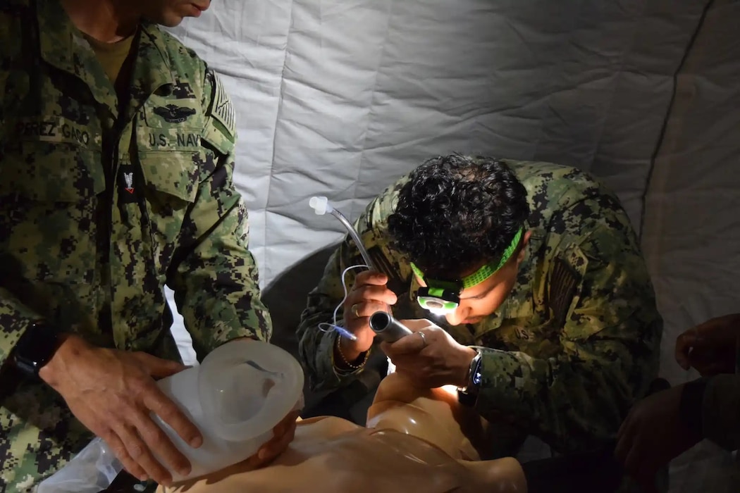 250501-A-ZZ123-1882 Army and Navy students in the Medical Education and Training Campus Respiratory Therapist course conduct a Joint Field Training Exercise on Joint Base San Antonio-Camp Bullis, Texas. After Hospital Corpsman 3rd Class Israel Perez pre-oxygenates the simulated patient, Hospital Corpsman 3rd Class Brandon Greco starts to intubate the ""patient" to secure the airway and begin ventilation