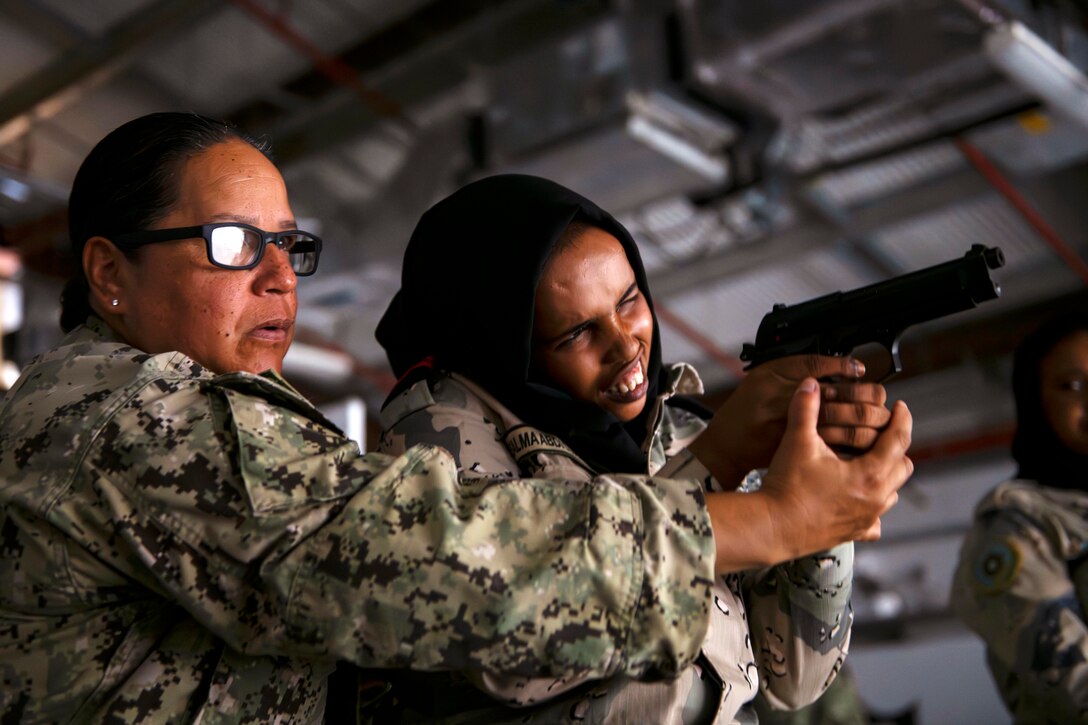 A U.S. sailor helps a Djiboutian service member aim a weapon.