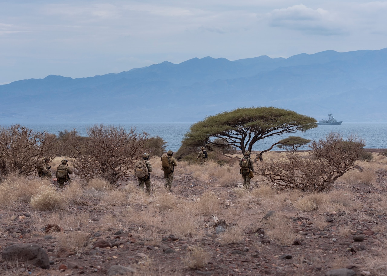 Spanish service members walk in a desert-like area with mountains in the distance.