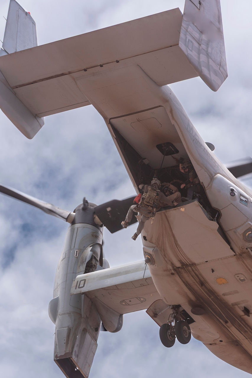 An airman is hoisted by an aircraft against a cloudy, blue sky.