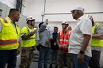 A group of men in reflective safety vests speak to each other.