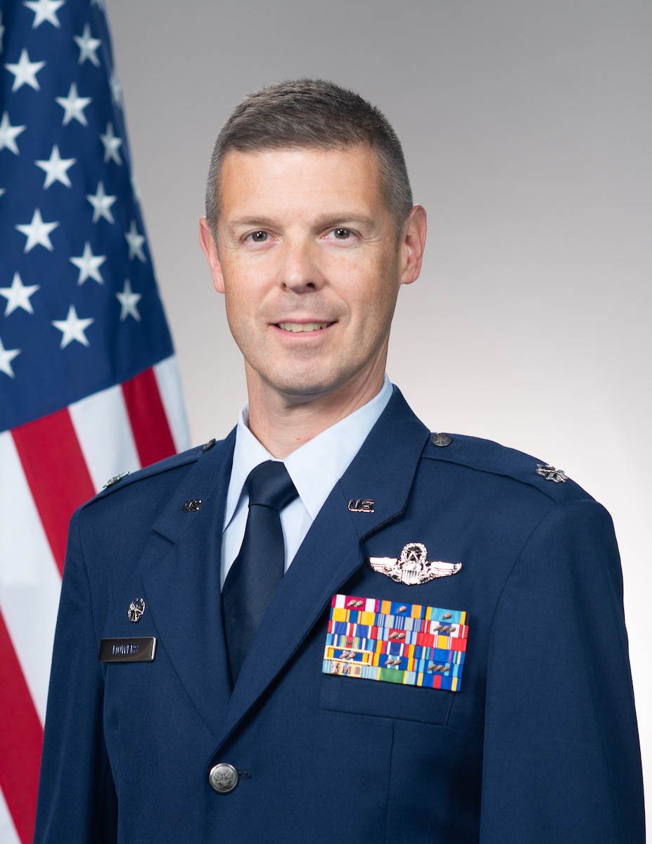 Lt. Col Mowers stands next to flag for official portrait in dress blues uniform.