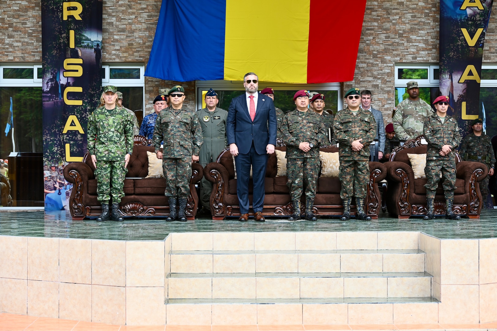 A formation of people in military uniforms stand with man in a dark blue suit in the center.