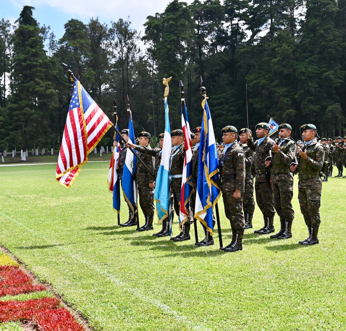A formation of people in military uniforms hold national flags.