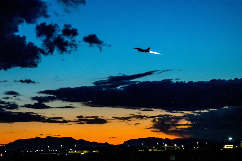 An Air Force jet leaves a contrail while flying in a vivid blue and orange cloud-streaked sky.