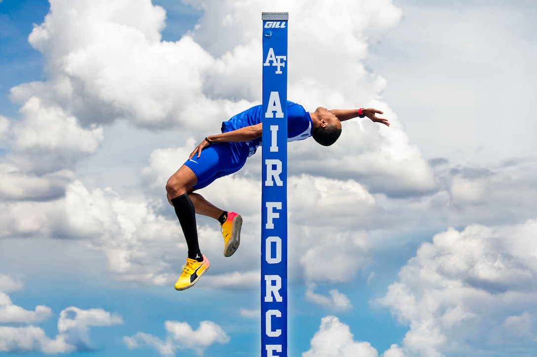 An athlete leans back while jumping in front of a blue post with blue skies and clouds in the background.
