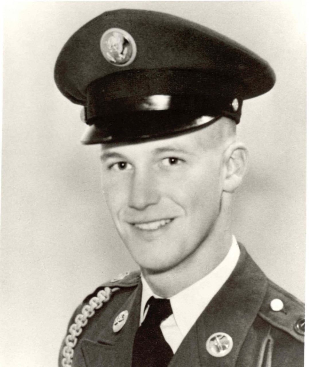 A man in uniform and cap smiles for a photo.