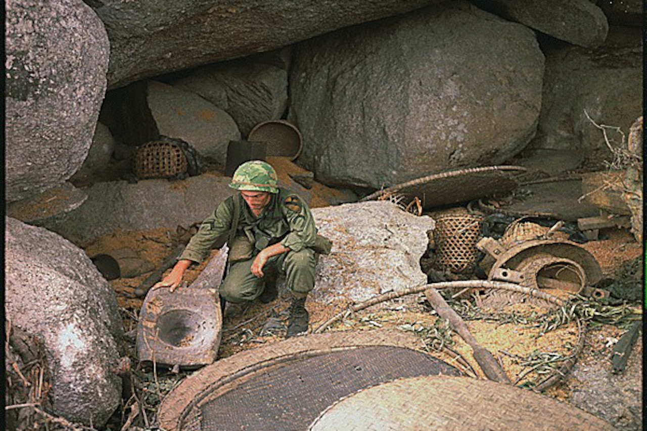 A man squats down beside large boulders.
