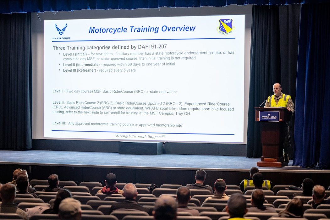 A large projector screen with motorcycle training objectives with a military member in a neon yellow safety vest