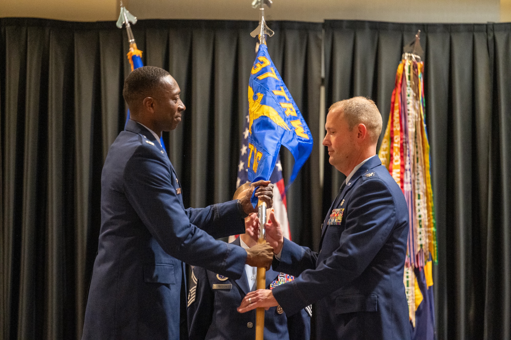 Col. Will Cooper, 37th Training Wing commander, passes the guidon to Col. Brian Caruthers during the 937th Training Group Assumption of Command on May 13, 2025, at Joint Base San Antonio-Fort Sam Houston, Texas. The 937th Training Group is responsible for training 19 Air Force Medical Specialties across four squadrons and 39 geographically separated locations, offering 68 formal courses to develop the next generation of medical professionals. (U.S. Air Force photo by 2nd Lt. Kate Anderson)