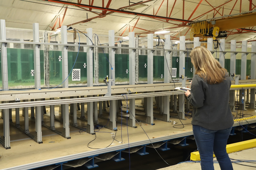 A researcher at the U.S. Army Engineer Research and Development Center observes sediment as it moves down a slope through water in a flume mounted on top of a tilt table.