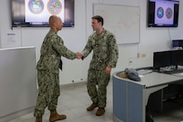 Two Navy personnel shake hands before a brief in a classroom.