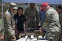Airmen and civilians view security forces equipment on a table.