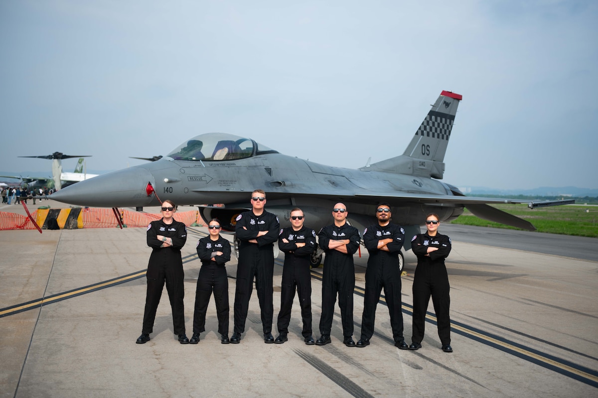military members pose in front of an F-16 fighter jet