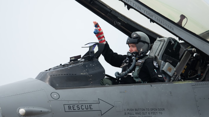 an F-16 fighter pilot gestures an engine start from his cockpit