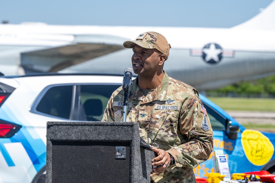 Col. Starks stand behind a podium and microphone, and aircraft with the Air Force star logo can be seen in the background
