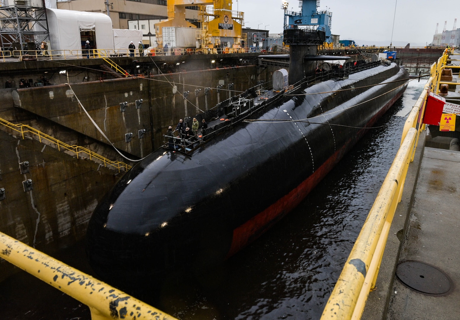 A large dark colored submarine sits in a dry dock.