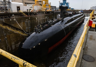 A large dark colored submarine sits in a dry dock.