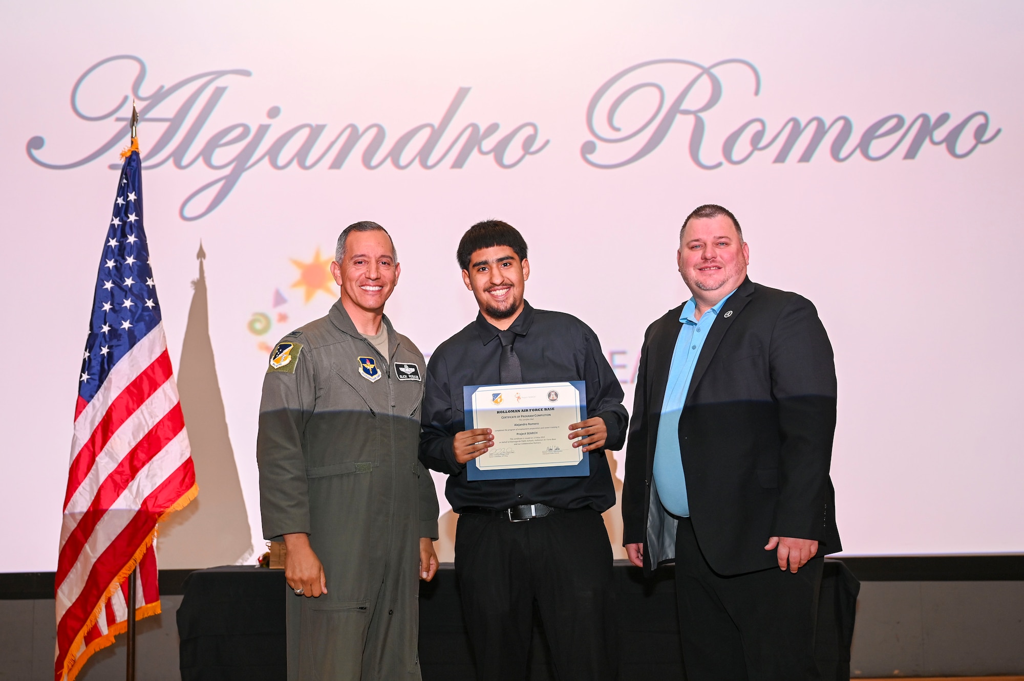 Alejandro Romero, Project SEARCH intern, center, accepts a graduation certificate from U.S. Air Force Col. Alfred Rosales 49th Wing deputy commander, for completing the program at Holloman Air Force Base, New Mexico, May 13, 2025. Project SEARCH is a high school transition program that provides training and education leading to employment for students with developmental disabilities. (U.S. Air Force photo by Senior Airman Michelle Ferrari)