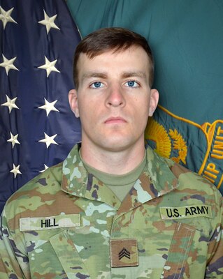 Man in U.S. Army uniform standing in front of two flags.