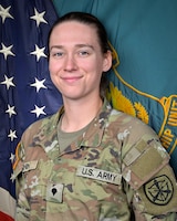 Woman in U.S. Army uniform standing in front of two flags.