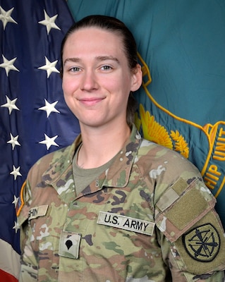 Woman in U.S. Army uniform standing in front of two flags.