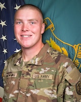 Man in U.S. Army uniform standing in front of two flags.