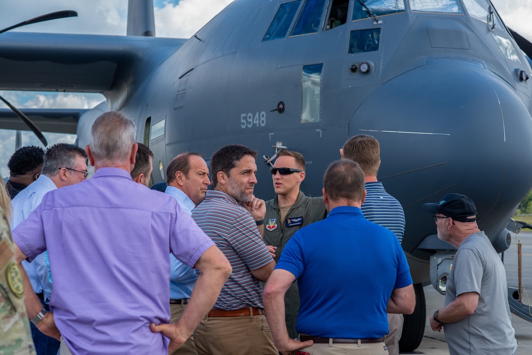 A group of people stand in front of a plane as a pilot speaks to them.