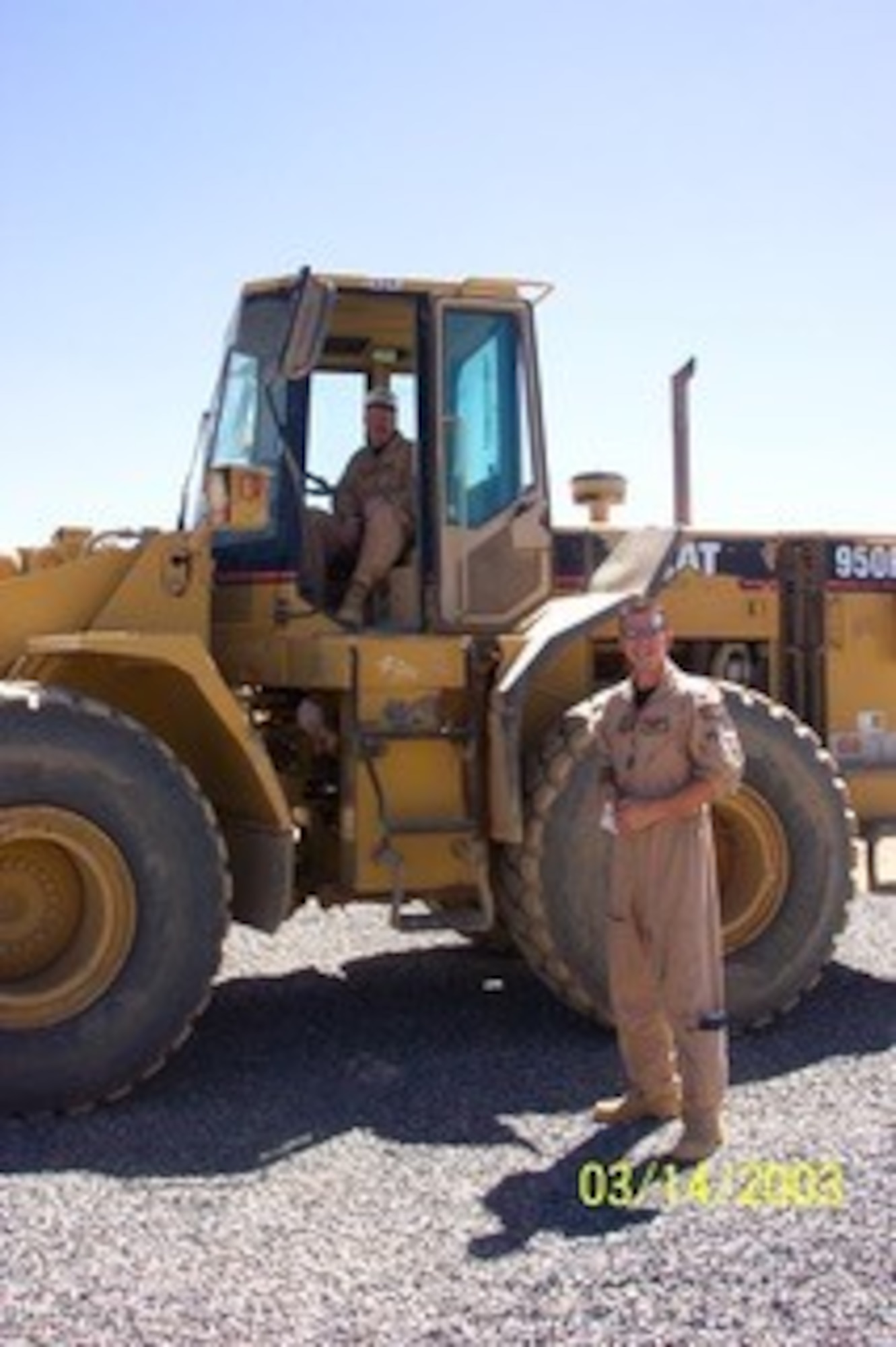 1st Lt. CJ Pfeil and his father, SMSgt Christopher Pfeil pose with heavy equipment while building up the base during a 2003 deployment to Tabuk, Saudi Arabia. Both the Pfeils used their construction background to build up the base for 4,000 people in between sorties. (US. Air Force courtesy photo)