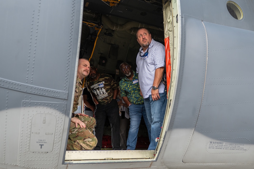 4 men stand looking out a planes side door.