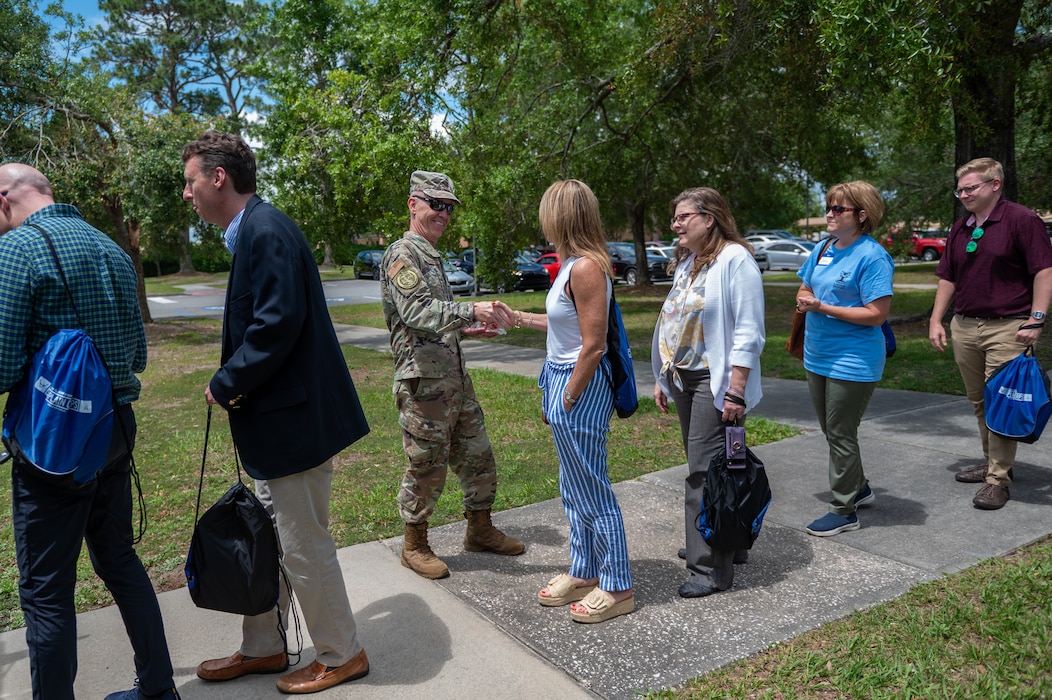 A row of people stand as they prepare to board a bus. Near the center of the photo a woman is seen shaking hands with a man in an Air Force uniform.