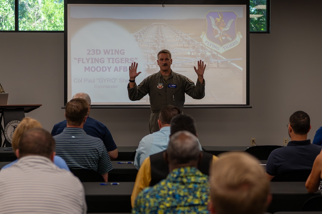 A man stands with hands raised, speaking to a group of people.