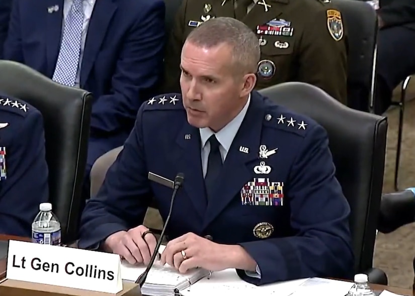 A man in a military uniform sits at a table and speaks to a panel.
