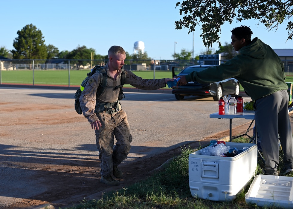 U.S. Air Force Airman 1st Class Wayne Knowlton-Thibeaux gives a bottle of a sports beverage to a 2025 Norwegian Foot March participant during the NFM at Goodfellow Air Force Base, Texas, May 3, 2025. Competitors must endure a distance of 18.6 miles while wearing a rucksack weighing a minimum of 24.25 lbs. at the start and finish of the event. (U.S. Air Force photo by Senior Airman Evelyn J. D’Errico)