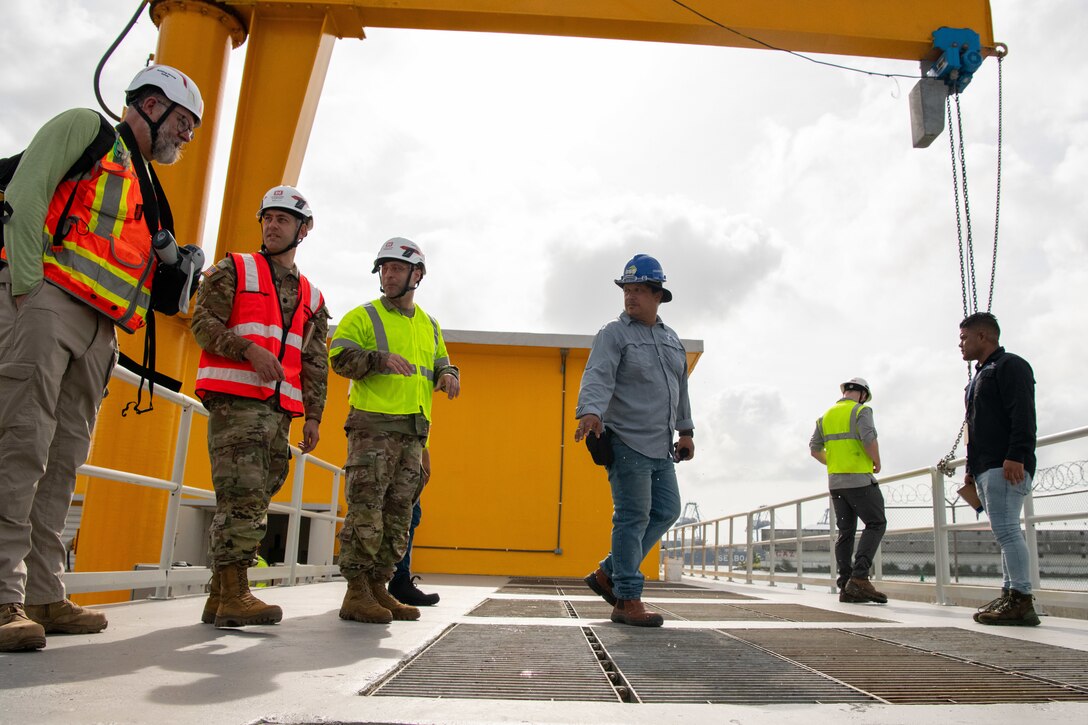 Members of the Army Corps of Engineer’s Forward Engineer Support Team talk in small groups. Some are wearing hard hats and reflective vests