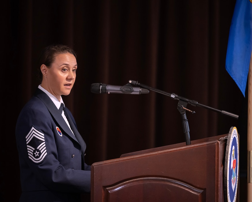 A woman in uniform with eight stripes on her sleeve stands behind a podium facing towards the right.