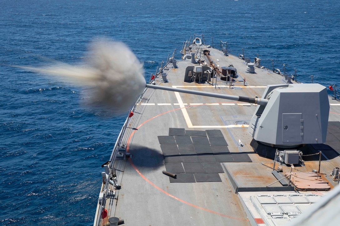 A projectile shoots from a gun on ship, creating a smoke cloud over blue water.
