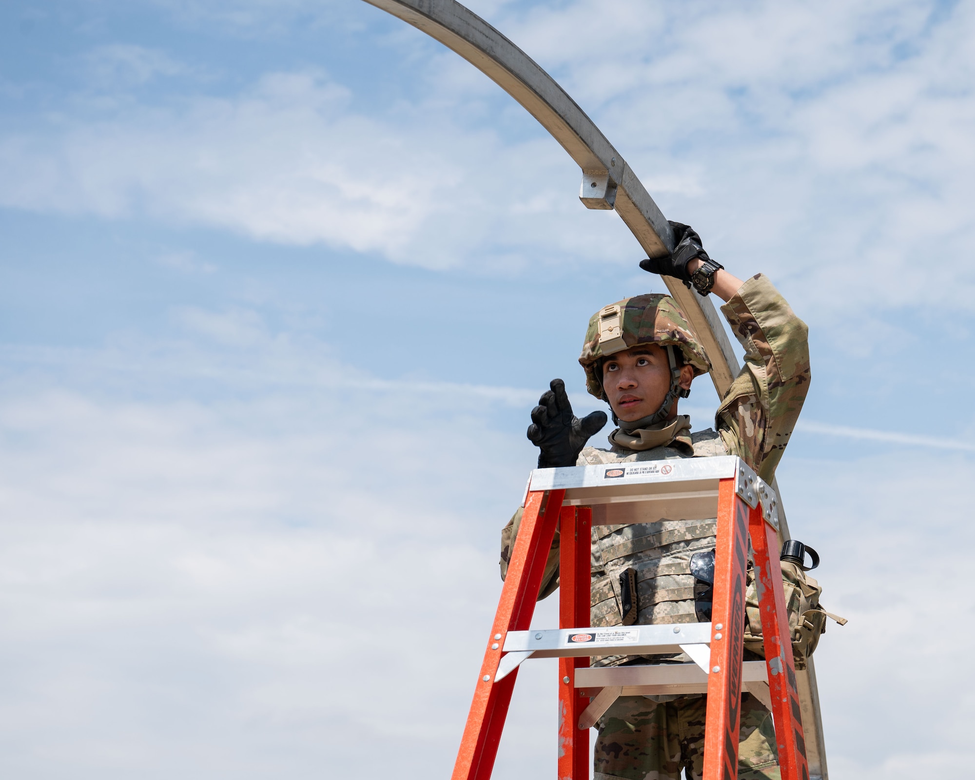 Airman stands on a ladder to set up a tent.