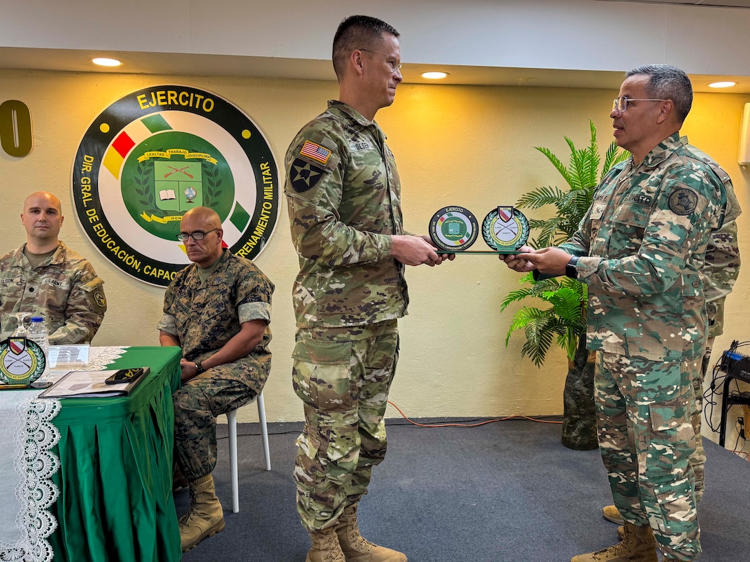 A man in a camouflage military uniform hand a certificate to another military person.