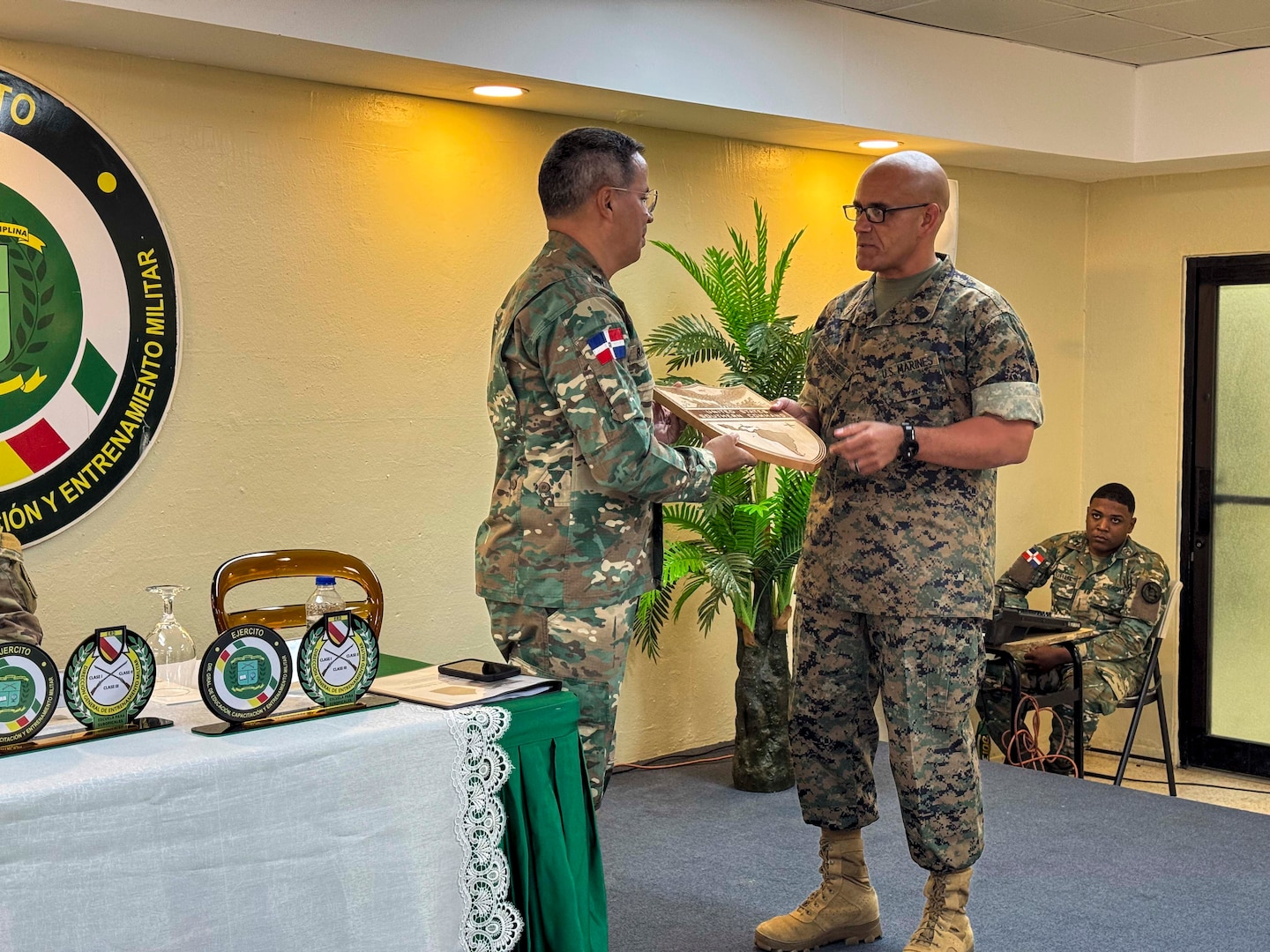 A man in a camouflage military uniform hand a plaque to another military person.