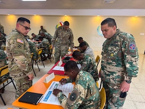 Military personnel sit at desks.