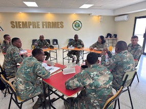 Military personnel sit at desks.