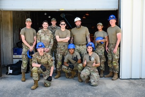 A group of Airmen wearing military uniforms and hard hats, stand and kneel for a photo.