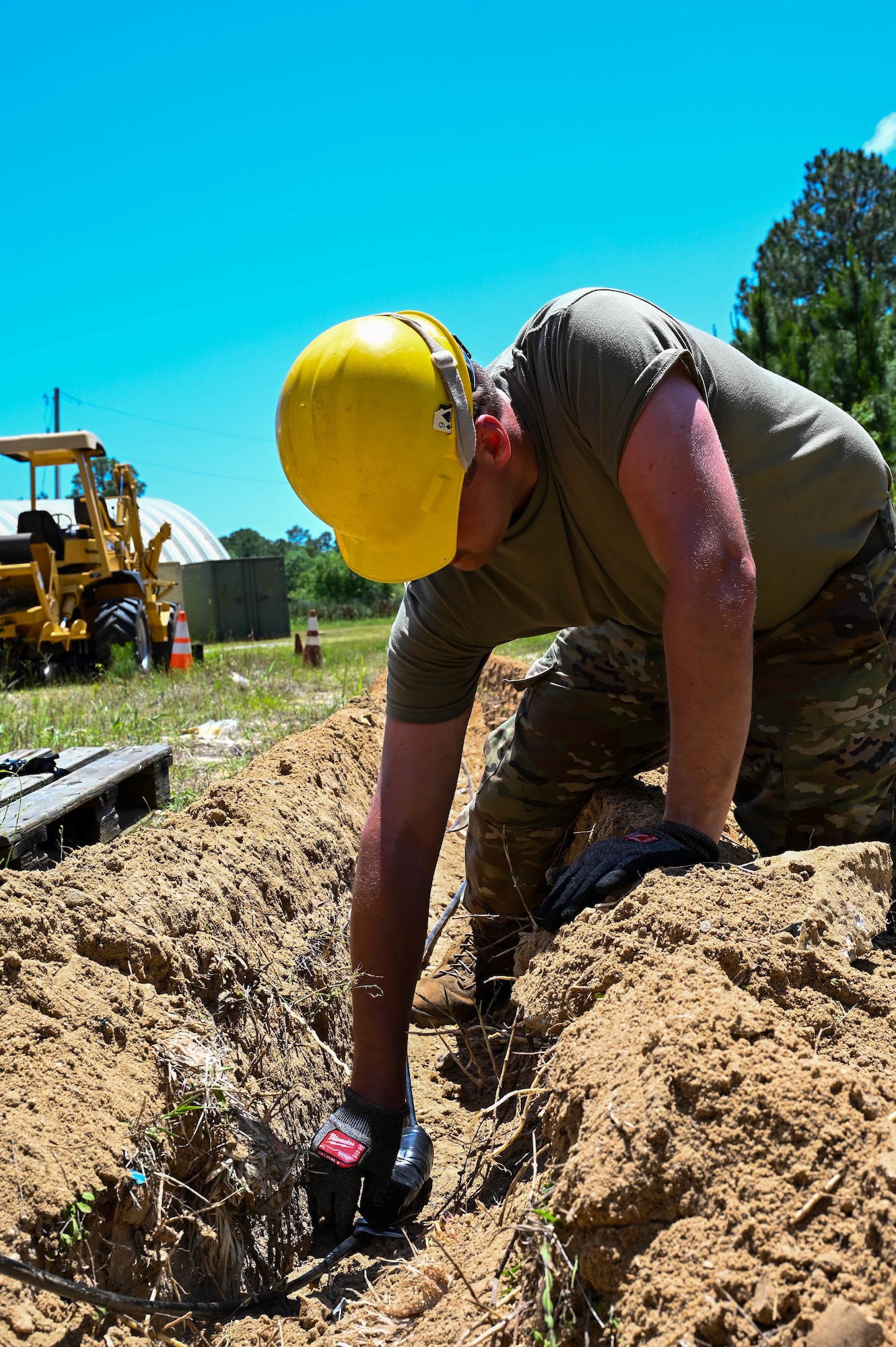 An Airman wearing military uniform lays fiber optic cable..