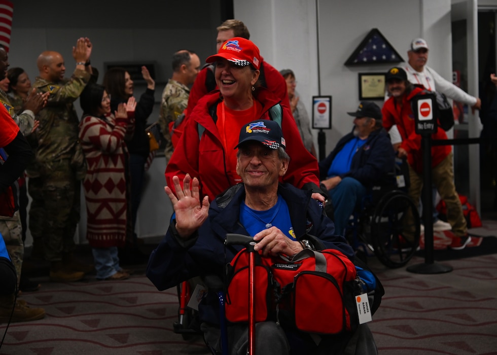 veterans in red white and blue and military members all cheering and welcoming home veterans from the honor flight