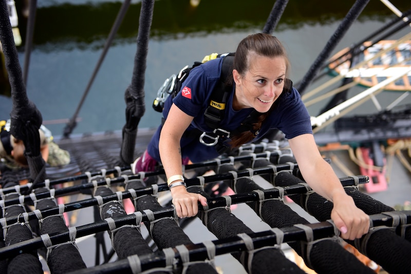 A sailor climbs up the shrouds on an old ship.