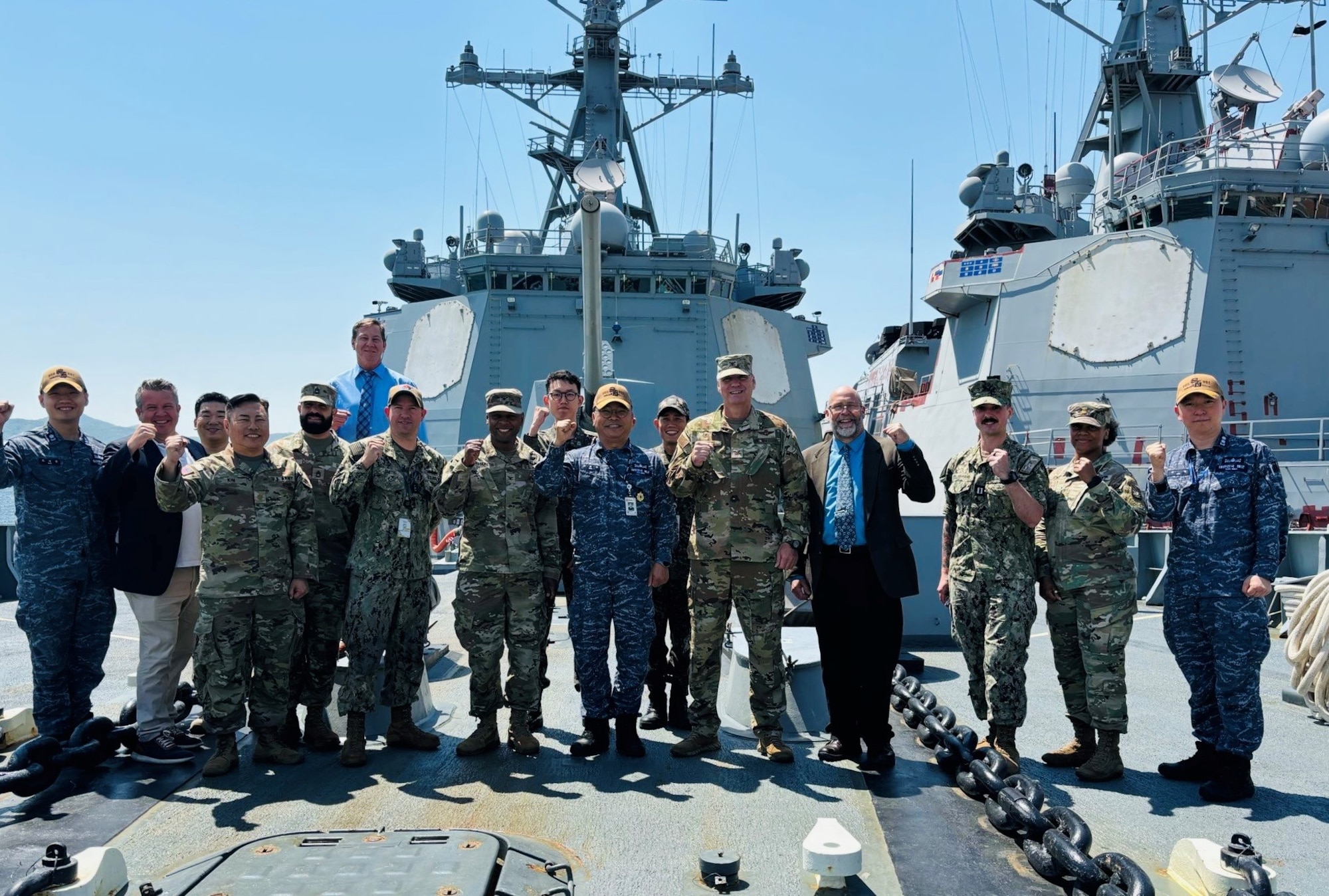 A line of uniformed men stand on the forward deck of a military ship