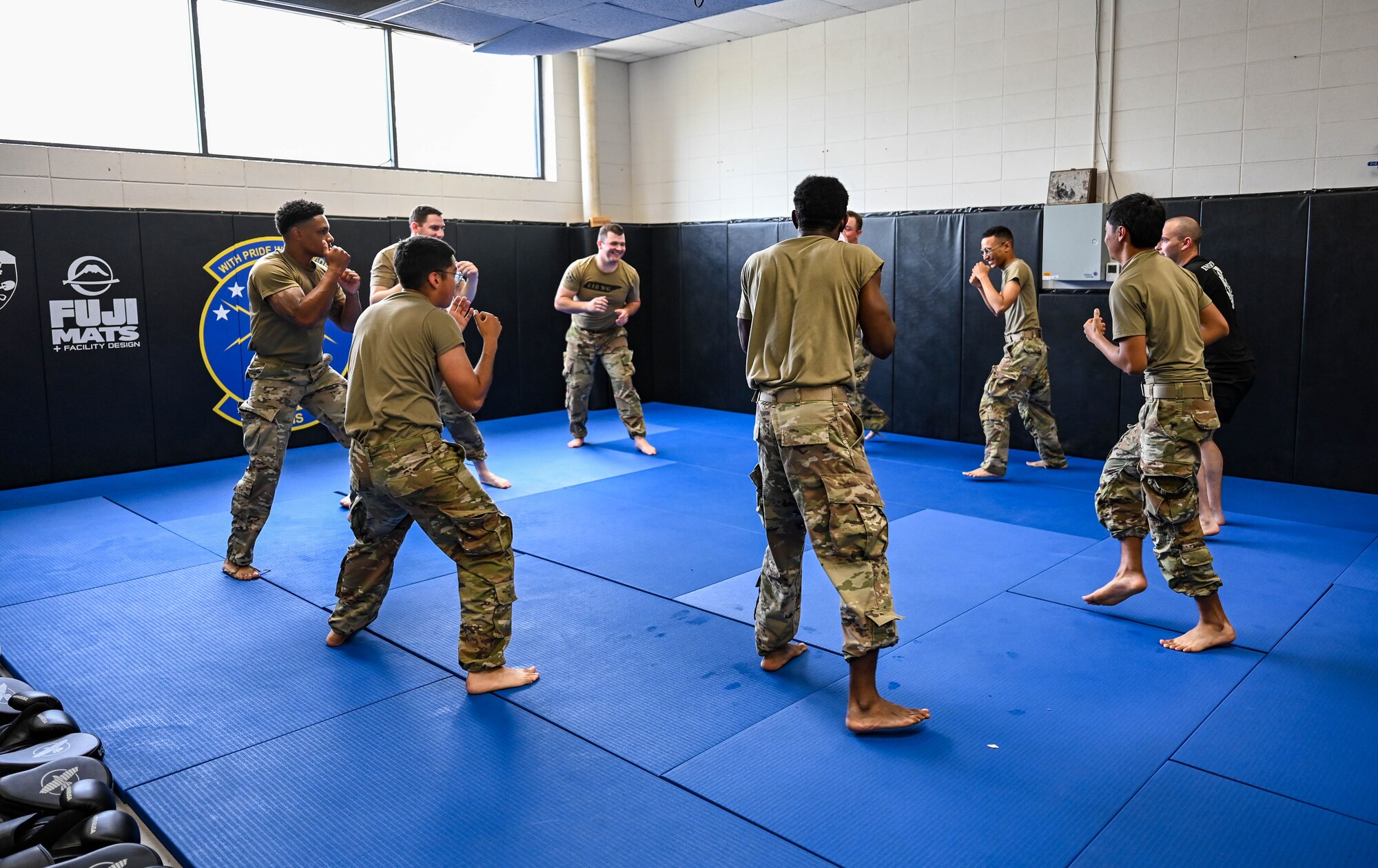 A group of Airmen, wearing military uniforms, stand in a circle, with arms in a defensive position in front of them, while being taught combatives.